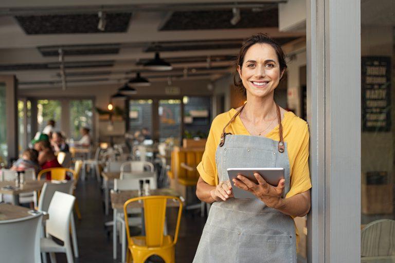 一名女企业主站在咖啡店外，手里拿着平板电脑